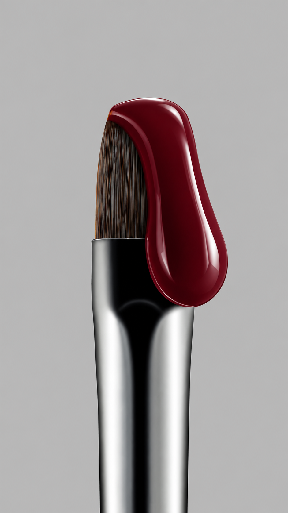 Makeup brush holding a glossy deep burgundy gel drop against a grey background